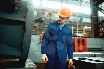 Worker in uniform and helmet on metelworking factory. Industrial production, metalwork engineering, power machines manufacturing