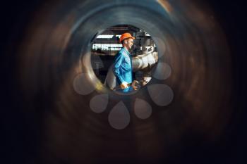 Worker with wrench on factory, view through the tube. Industrial production, metalwork engineering, power machines manufacturing