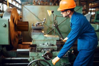 Worker in uniform and helmet works on lathe, factory. Industrial production, metalwork engineering, power machines manufacturing