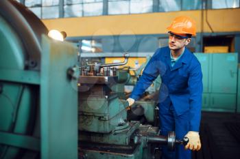 Worker in uniform and helmet works on lathe, factory. Industrial production, metalwork engineering, manufacturing