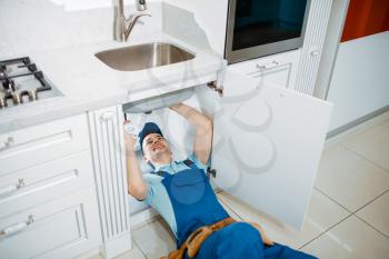 Male plumber in uniform installing drain pipe in the kitchen. Handywoman with toolbag repair sink, sanitary equipment service at home
