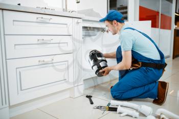 Male plumber in uniform installing disposer in the kitchen. Handywoman with toolbag repair sink, sanitary equipment service at home