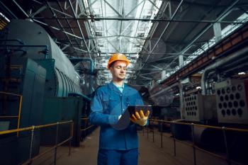 Male worker holds notebook, factory interior on background, plant. Industrial production, metalwork engineering, power machines manufacturing