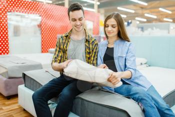 Young love couple choosing pillow in furniture store showroom. Man and woman looking samples for bedroom in shop, husband and wife buys goods for modern home interior