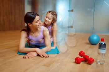 Mother and daughter lying on mat together in gym, fitness workout, gymnastic. Mom and little girl in sportswear, joint training in sport club