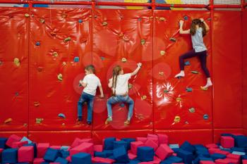 Children on climbing wall in the entertainment center. Girls and boy leisures on holidays, childhood happiness, happy kids on playground