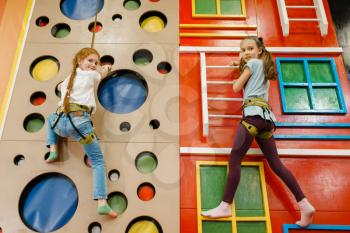 Little girlfriends on climbing wall in the entertainment center. Female children leisures on holidays, childhood happiness, happy kids on playground