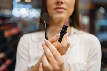 Woman shows lipstick and liner in cosmetics store. Buyer at the showcase in luxury beauty shop salon, female customer in fashion market