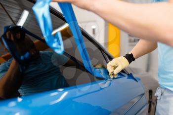 Male mechanic hands installs protective vinyl foil or film on vehicle door. Worker makes auto detailing. Automobile paint protection, professional tuning