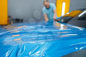 Male car wrapper puts protective vinyl foil or film on hood. Worker makes auto detailing. Automobile paint protection coating, professional tuning
