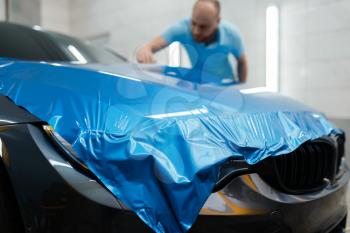Car wrapping, man installs protective vinyl foil or film on hood. Worker makes auto detailing. Automobile paint protection coating, professional tuning