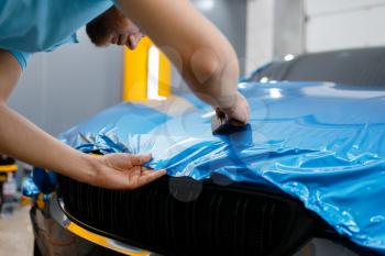 Male car wrapper puts protective vinyl foil or film on hood. Worker makes auto detailing. Automobile paint protection coating, tuning