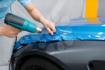 Car wrapping, mechanic with drier installs protective vinyl foil or film on vehicle hood. Worker makes auto detailing. Automobile paint protection coating, professional tuning