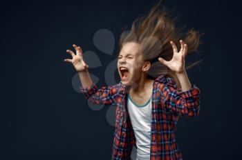 Little girl screams in studio, developing hairstyle effect. Children and wind, kid isolated on dark background, child emotion