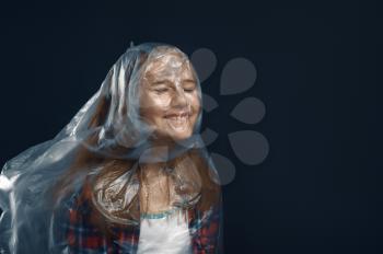 Little girl wrapped in film standing against powerful airflow in studio, developing hairstyle effect. Children and wind, kid isolated on dark background, child emotion