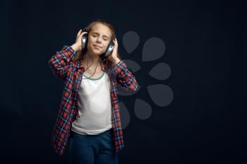 Little girl in headphones against powerful airflow in studio, developing hair effect. Children and wind, kid isolated on dark background, child emotion