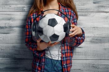 Little girl puts headphones on ball in studio. Children and gadgets, kid isolated on wooden background, child emotion, schoolgirl photo session