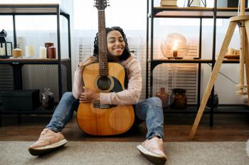Cheerful woman sitting on the floor and hugs the guitar at home. Pretty lady with musical instrument relax in the room, female music lover resting