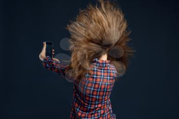 Little girl standing against powerful airflow in studio, back view, developing hairstyle effect. Children and wind, kid isolated on dark background, child emotion