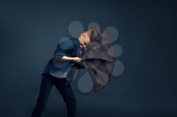 Little boy with a scared face holds an umbrella in studio, wind effect, powerful airflow. Children with developing hairs, kids isolated on dark background, child emotion