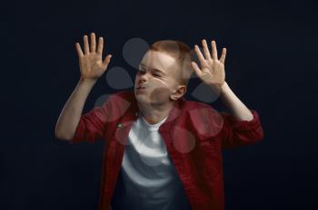 Schoolboy makes face leaning against the glass in studio. Happy childhood, children having fun, funny kid isolated on dark background, child emotion