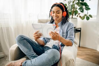 Woman in headphones listening to music from tablet pc. Pretty lady in earphones relax in the room, sound lover resting in armchair