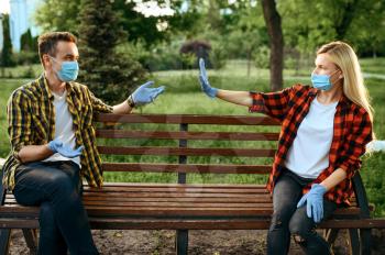 Young love couple in masks and gloves sitting on bench in park, quarantine. Romantic meeting during the epidemic, health care and protection, pandemic lifestyle