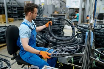 Worker at the assemly line holds bicycle tire on factory. Bike wheels production in workshop, cycle parts installation, modern technology