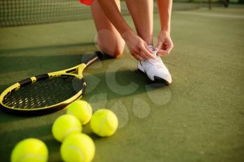 Female tennis player ties her shoelaces on outdoor court. Active healthy lifestyle, sport game competition, fitness training with racquet