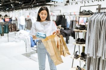 Cheerful woman puts clothes in bag, clothing store. Female person shopping in fashion boutique, shopaholic, shopper looking on garment