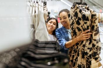 Two girls choosing dresses in clothing store. Women shopping in fashion boutique, shopaholics, shoppers looking garment on hangers