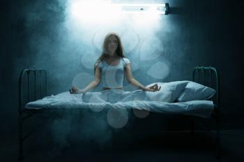 Psycho woman sitting in yoga pose in bed, dark room on background. Psychedelic person having problems every night, depression and stress, sadness, psychiatry hospital