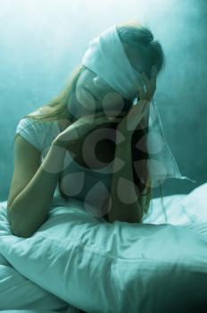 Blindfolded crazy woman sitting in bed, dark room on background. Psychedelic female person having problems every night, depression and stress, sadness, psychiatry hospital