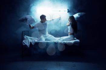 Psycho man and woman fights on pillows in bed, dark room on background. Psychedelic person having problems every night, depression and stress, sadness, psychiatry hospital