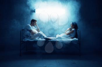 Crazy man and woman are sitting in bed, dark room on background. Psychedelics having problems every night, depression and stress, sadness, psychiatry hospital