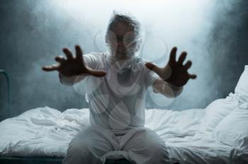 Crazy man held out his hands in bed, insomnia, dark smoky room on background. Psychedelic person having problems every night, depression and stress, sadness, psychiatry hospital