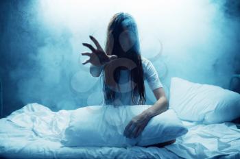 Crazy woman show hand in bed, insomnia, dark smoky room on background. Psychedelic person having problems every night, depression and stress, sadness, psychiatry hospital