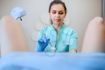 Female gynecologist holds cotton tampon, patient in chair. Gynecological examination in clinic, gynecology diagnostic or consultation, exam. Doctor and woman in hospital