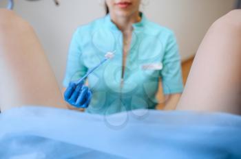 Female gynecologist holds cotton tampon, patient in chair. Gynecological examination in clinic, gynecology diagnostic or consultation, exam. Doctor and woman in hospital