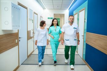 Three smiling doctors in uniform walking in clinic corridor. Professional medical specialist in hospital, laryngologist or otolaryngologist, gynecologist or mammologist, surgeon