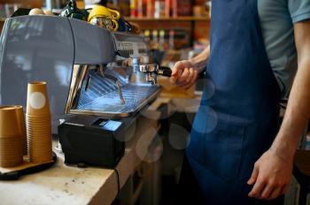 Male barista in apron prepares coffee on machine in cafe. Man makes fresh espresso in cafeteria, waiter at the counter in bar