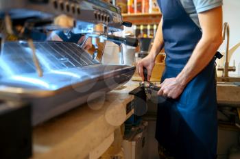 Male barista in apron prepares coffee on machine in cafe. Man makes fresh espresso in cafeteria, waiter at the counter in bar