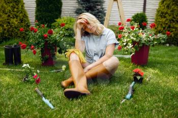 Tired woman sitting on the grass in the garden. Female gardener takes care of plants outdoor, gardening hobby, florist lifestyle and leisure