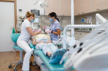 Female dentist and assistant works with patient in clinic, stomatology. Doctor in uniform, medical worker, medicine and health, professional teeth care, dentistry