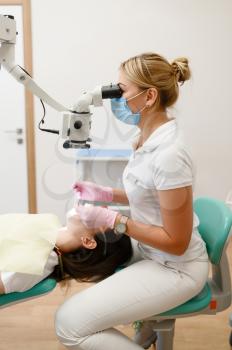 Female dentist treats patient tooth in clinic, stomatology. Doctor in uniform, medical worker, medicine and health, professional teeth care, dentistry