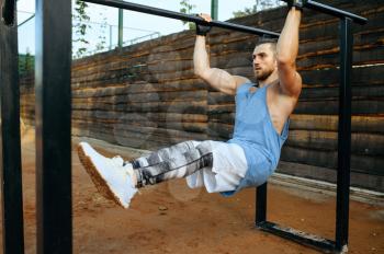Muscular man doing abs exercise on parallel bars, street workout. Fitness training on sports ground, male person pumps muscles, active urban lifestyle