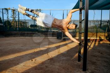 Muscular man hanging horizontally on a bar, street workout. Fitness training on sports ground, male person pumps muscles, active urban lifestyle