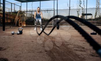 Strong man doing exercise with ropes, street workout, crossfit. Fitness training on sports ground outdoor, male person pumps muscles, active urban lifestyle