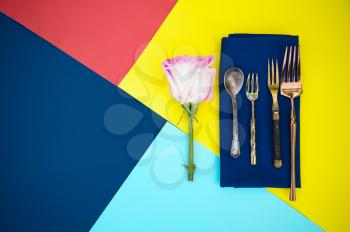 Table setting, flower and silverware on blue napkin closeup, top view, nobody. Banquet decoration, colorful tablecloth, tableware