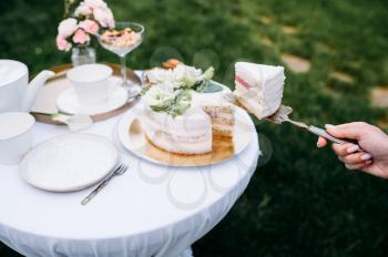 Table setting, tea party, female hand takes cake closeup, side view. Luxury silverware on white tablecloth, tableware outdoors